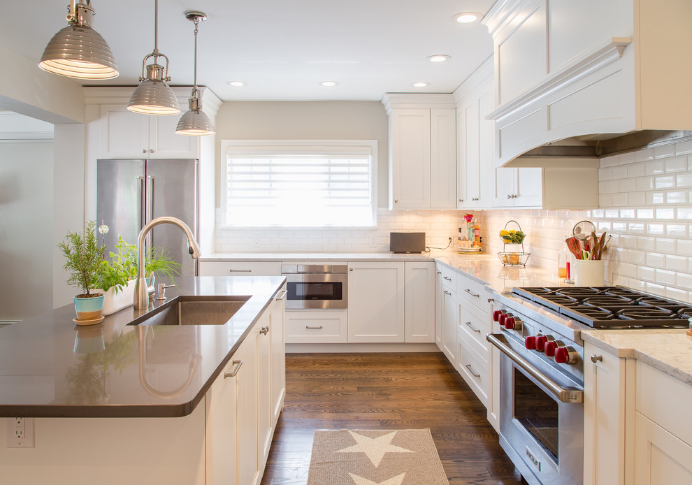 This is an example of a large contemporary l-shaped open plan kitchen in New York with a submerged sink, white cabinets, white splashback, metro tiled splashback, stainless steel appliances, dark hardwood flooring and an island.