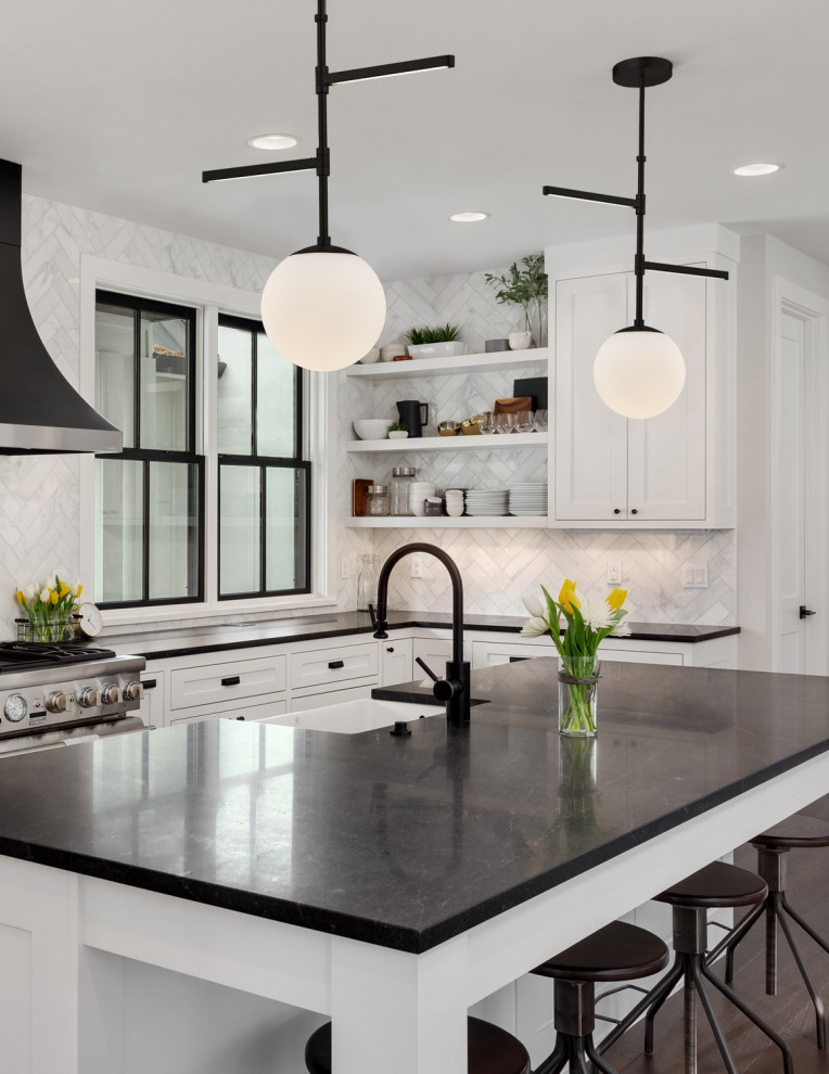 Example of a transitional l-shaped dark wood floor and brown floor kitchen design in Los Angeles with a farmhouse sink, shaker cabinets, white cabinets, white backsplash, stainless steel appliances, an island and black countertops