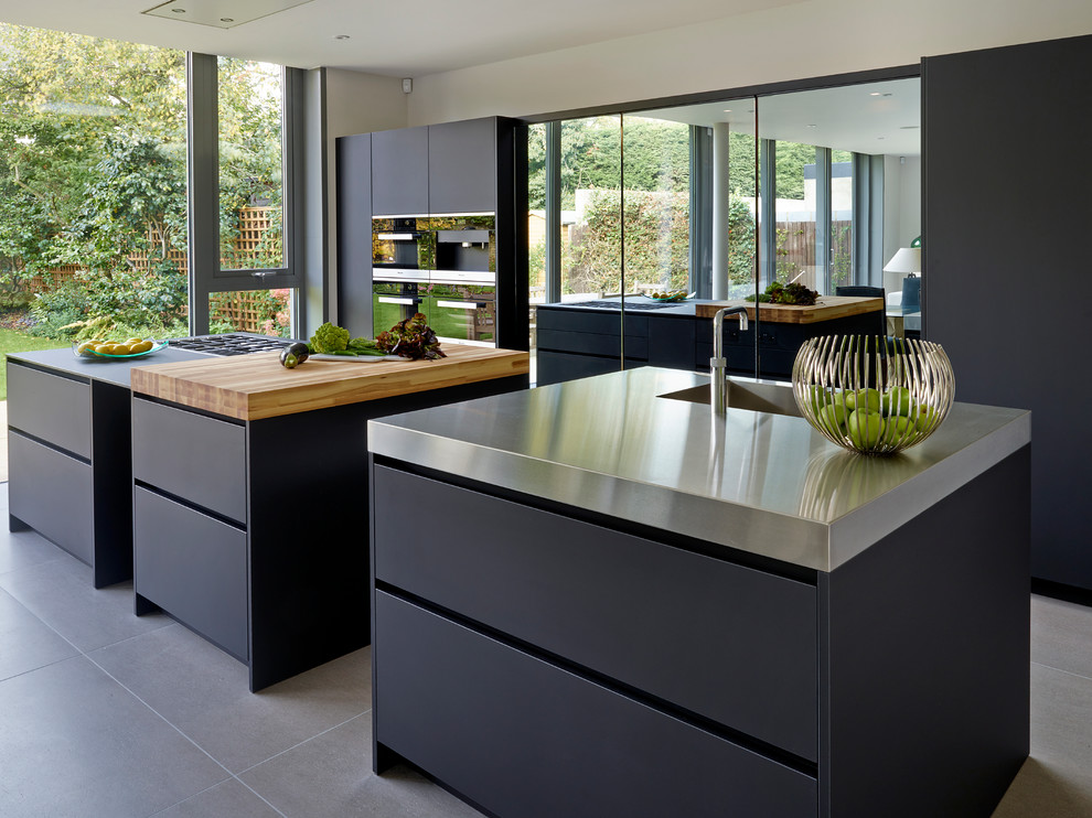 Diseño de cocina contemporánea con armarios con paneles lisos, puertas de armario negras, encimera de acero inoxidable, electrodomésticos de acero inoxidable y dos o más islas
