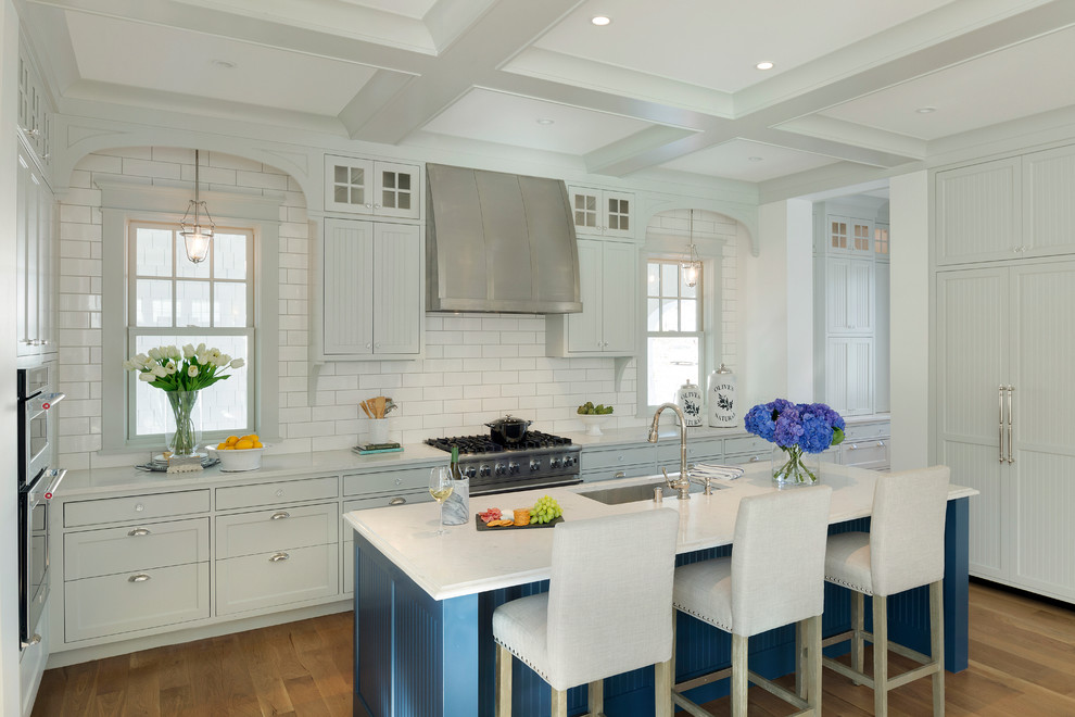 Eat-in kitchen - coastal galley light wood floor eat-in kitchen idea in Minneapolis with an undermount sink, recessed-panel cabinets, white cabinets, solid surface countertops, white backsplash, ceramic backsplash, stainless steel appliances and an island