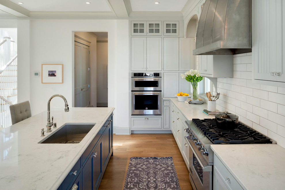 Inspiration for a coastal l-shaped medium tone wood floor kitchen remodel in Minneapolis with an undermount sink, shaker cabinets, gray cabinets, white backsplash, subway tile backsplash, stainless steel appliances and an island