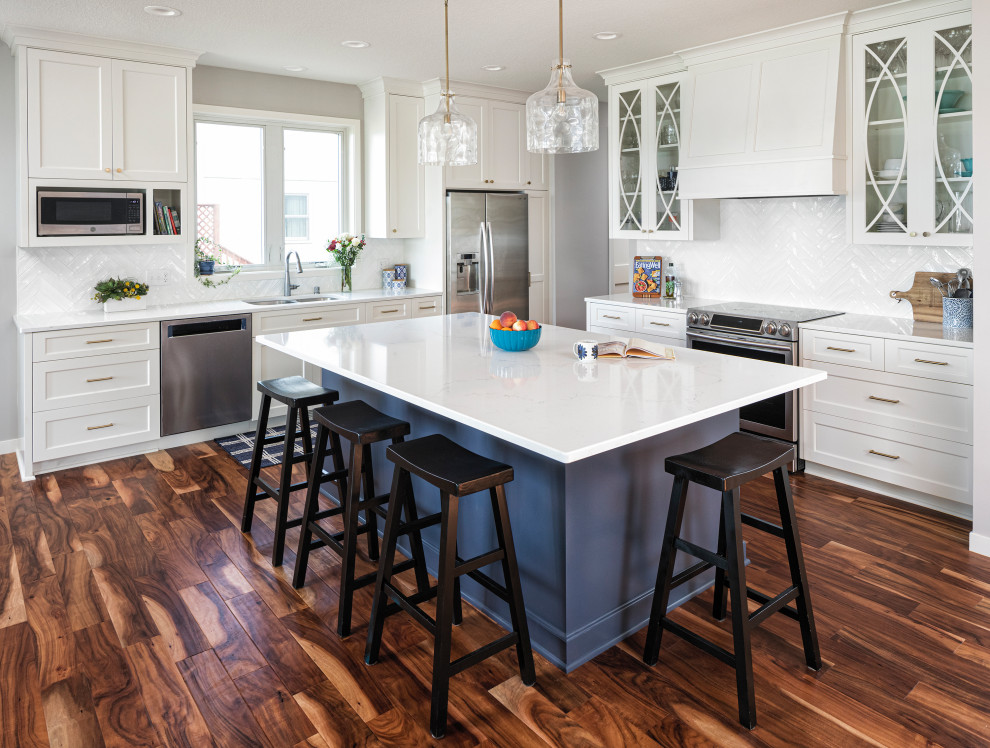Inspiration for a mid-sized coastal l-shaped medium tone wood floor eat-in kitchen remodel in Minneapolis with flat-panel cabinets, white cabinets, quartz countertops, white backsplash, ceramic backsplash, stainless steel appliances, an island and white countertops