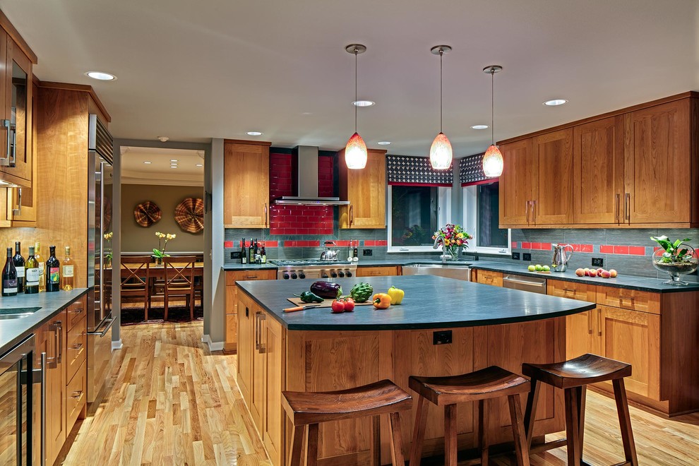 Photo of a large contemporary u-shaped open plan kitchen in Seattle with a belfast sink, shaker cabinets, medium wood cabinets, soapstone worktops, red splashback, ceramic splashback, stainless steel appliances, light hardwood flooring, an island, brown floors and blue worktops.