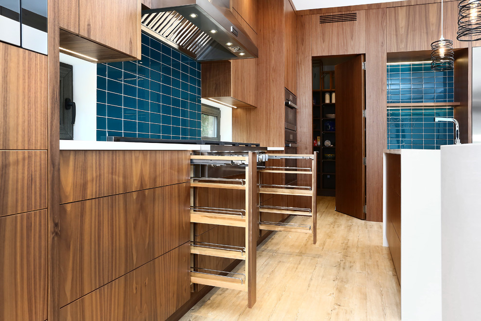 Inspiration for an expansive world-inspired l-shaped kitchen/diner in Vancouver with a built-in sink, flat-panel cabinets, light wood cabinets, engineered stone countertops, blue splashback, glass tiled splashback, stainless steel appliances, bamboo flooring, multiple islands and grey floors.