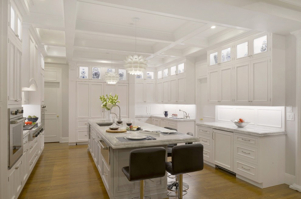 Exempel på ett mycket stort klassiskt u-kök, med en undermonterad diskho, vita skåp, bänkskiva i kvartsit, vitt stänkskydd, rostfria vitvaror, mellanmörkt trägolv, en köksö och luckor med infälld panel