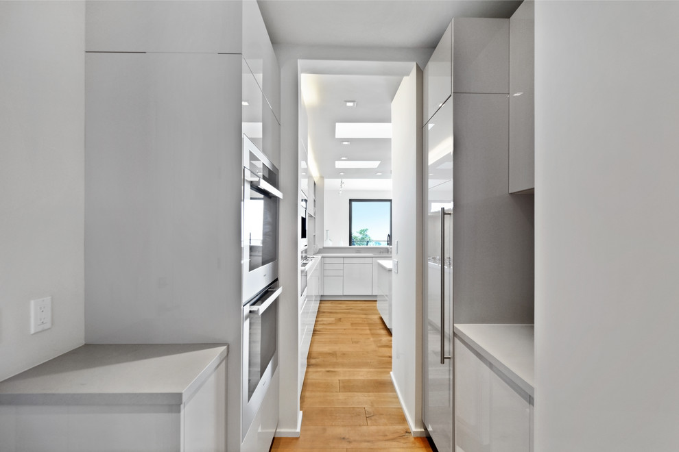 This is an example of a large contemporary kitchen pantry in Other with a submerged sink, flat-panel cabinets, beige cabinets, multi-coloured splashback, stone slab splashback, integrated appliances, medium hardwood flooring and an island.