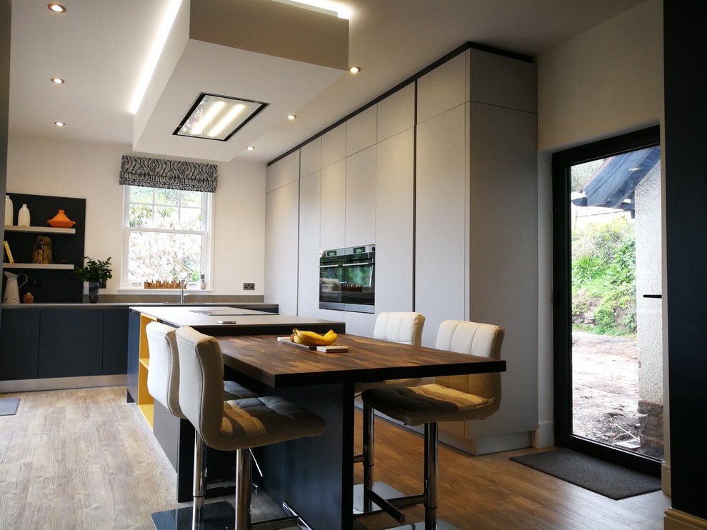 Inspiration for a large contemporary l-shaped open plan kitchen in Other with an integrated sink, flat-panel cabinets, grey cabinets, composite countertops, grey splashback, stainless steel appliances, vinyl flooring, an island, brown floors and grey worktops.