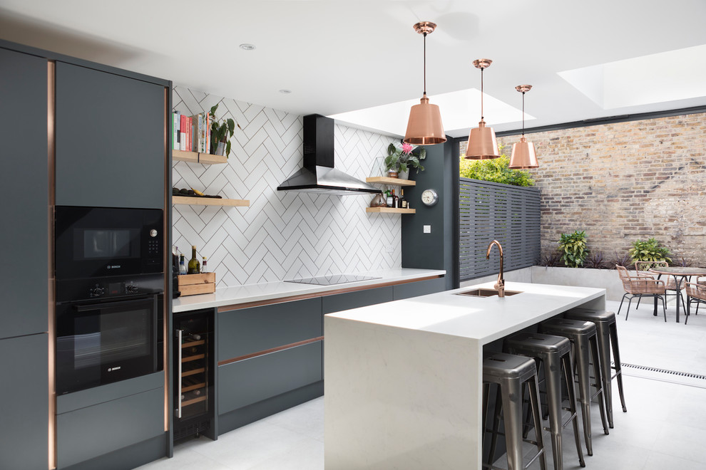 Design ideas for a medium sized contemporary single-wall kitchen/diner in London with a submerged sink, flat-panel cabinets, blue cabinets, quartz worktops, white splashback, metro tiled splashback, black appliances, an island, grey floors and white worktops.
