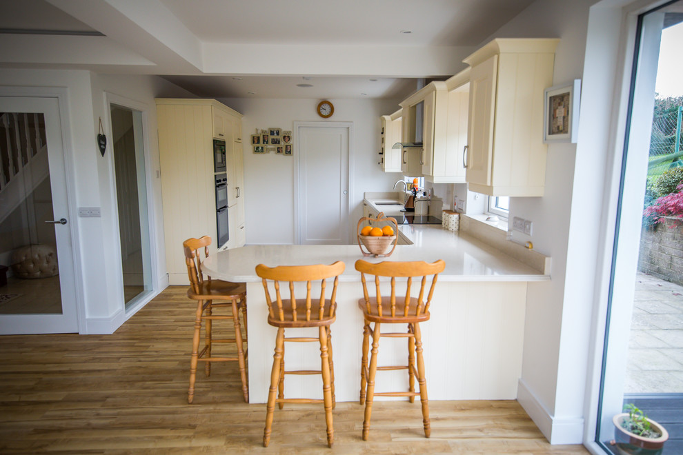 Foto de cocinas en L clásica renovada con salpicadero de azulejos de vidrio, electrodomésticos con paneles, suelo de madera clara y península