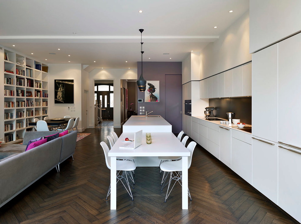 На фото: параллельная кухня-гостиная в современном стиле с плоскими фасадами, белыми фасадами, черным фартуком, темным паркетным полом и островом