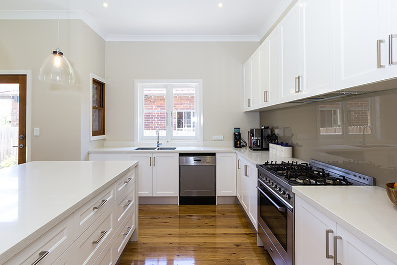 Modern inredning av ett kök, med en undermonterad diskho, luckor med infälld panel, bänkskiva i kvarts, brunt stänkskydd, glaspanel som stänkskydd och rostfria vitvaror