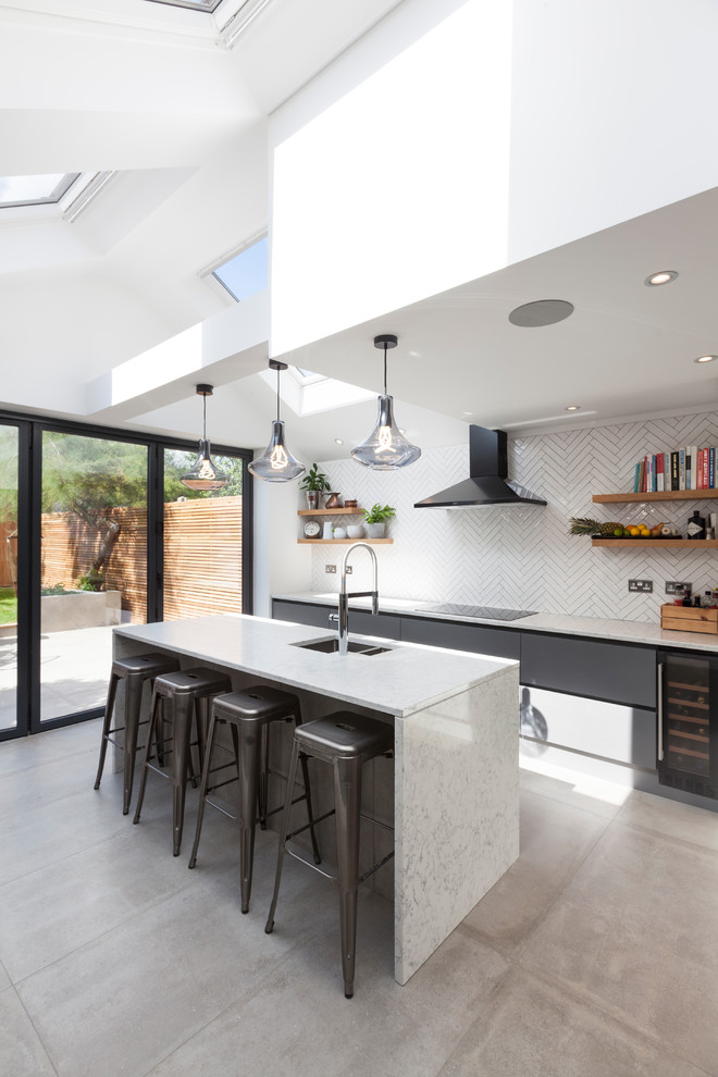 This is an example of a medium sized contemporary single-wall open plan kitchen in London with a submerged sink, flat-panel cabinets, grey cabinets, white splashback, metro tiled splashback, an island and grey floors.