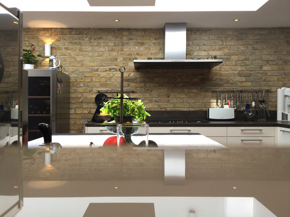 На фото: кухня-гостиная в современном стиле с плоскими фасадами, белыми фасадами, черным фартуком и полуостровом