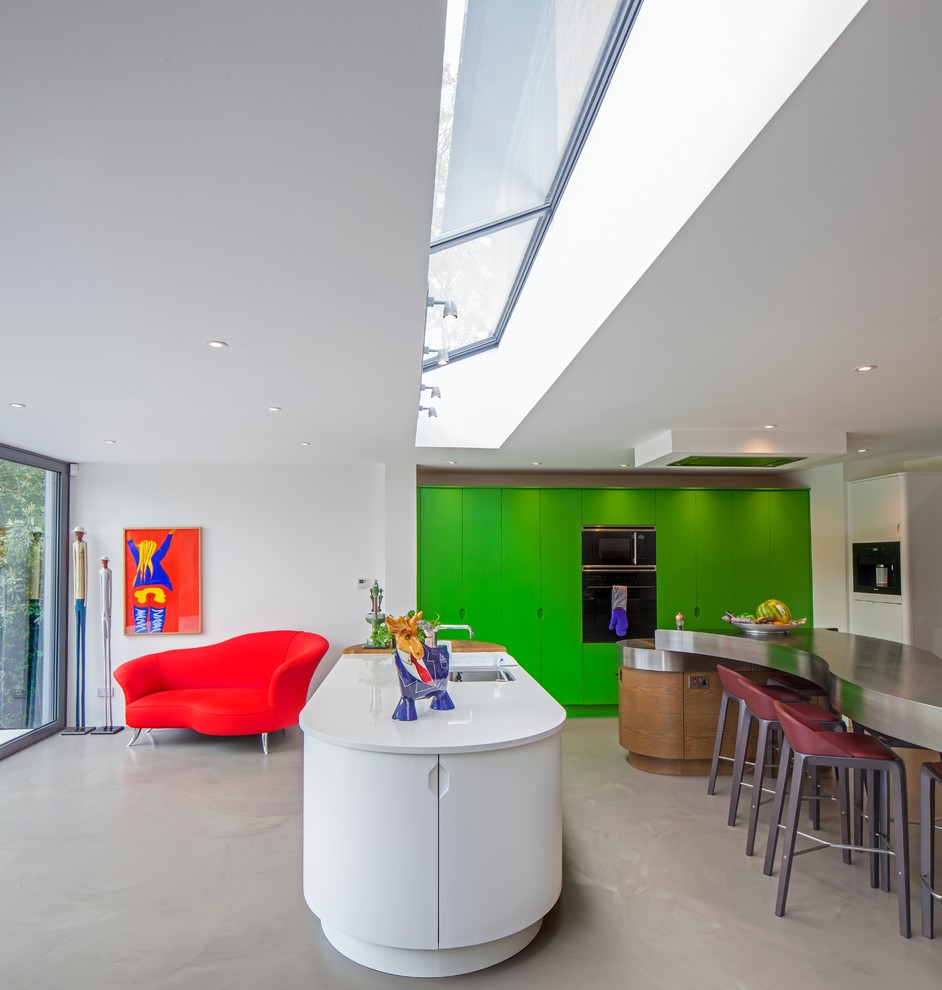 Moderne Küche in U-Form mit flächenbündigen Schrankfronten, grünen Schränken, Edelstahl-Arbeitsplatte, Elektrogeräten mit Frontblende, Betonboden, zwei Kücheninseln und Unterbauwaschbecken in Hertfordshire