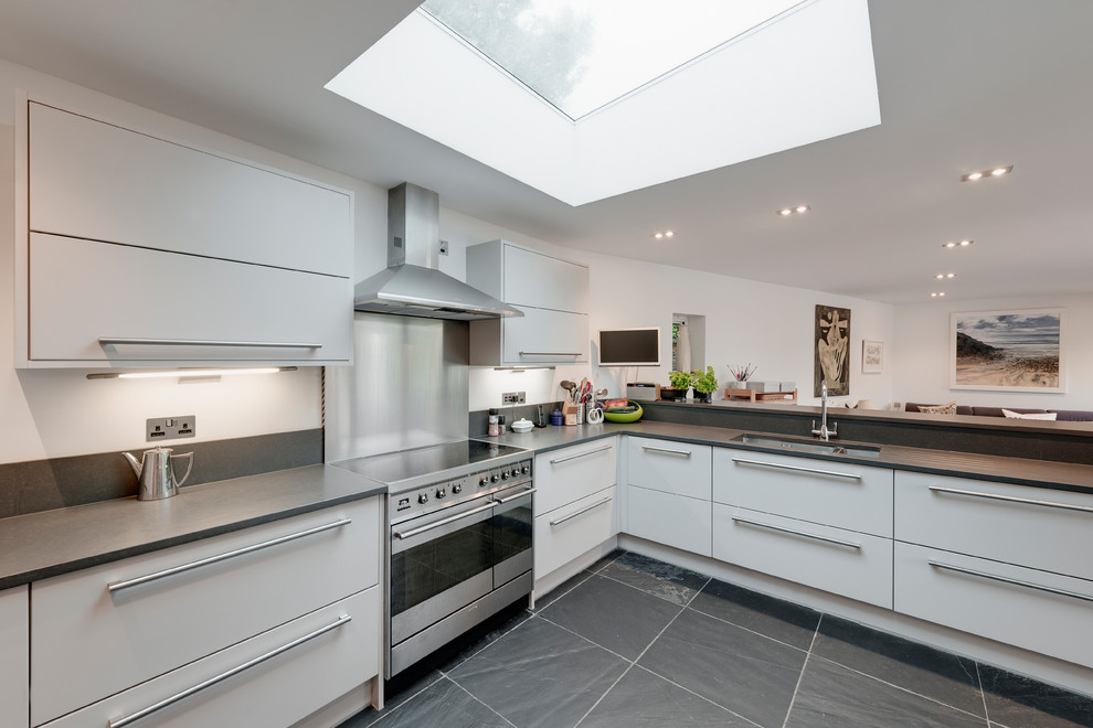 Photo of a medium sized modern u-shaped open plan kitchen in Cornwall with an integrated sink, flat-panel cabinets, white cabinets, composite countertops, grey splashback, slate splashback, stainless steel appliances, slate flooring, an island and grey floors.