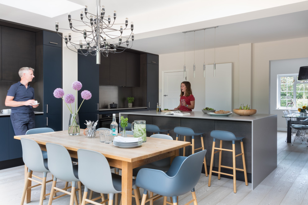 Eat-in kitchen - large contemporary medium tone wood floor and gray floor eat-in kitchen idea in Sussex with a drop-in sink, flat-panel cabinets, dark wood cabinets, solid surface countertops, metallic backsplash, stainless steel appliances, an island and gray countertops