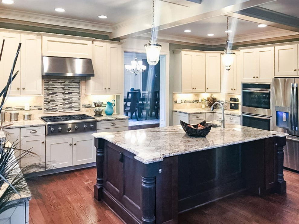 Example of a large classic u-shaped dark wood floor, brown floor and exposed beam open concept kitchen design in Cleveland with a farmhouse sink, shaker cabinets, white cabinets, granite countertops, multicolored backsplash, limestone backsplash, stainless steel appliances, an island and multicolored countertops