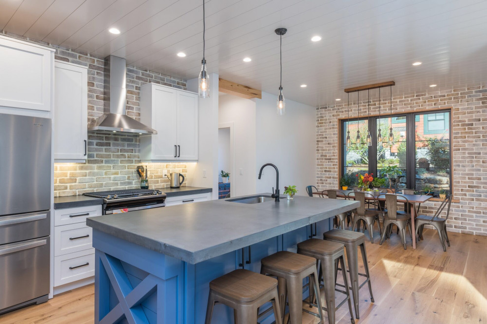 Mid-sized transitional l-shaped light wood floor and brown floor eat-in kitchen photo in Other with an undermount sink, recessed-panel cabinets, white cabinets, concrete countertops, gray backsplash, brick backsplash, stainless steel appliances, an island and gray countertops