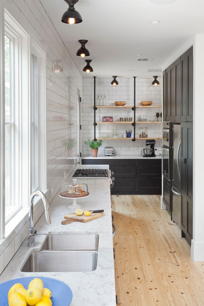 Foto på ett lantligt kök, med en dubbel diskho, öppna hyllor, vitt stänkskydd, stänkskydd i tunnelbanekakel och ljust trägolv