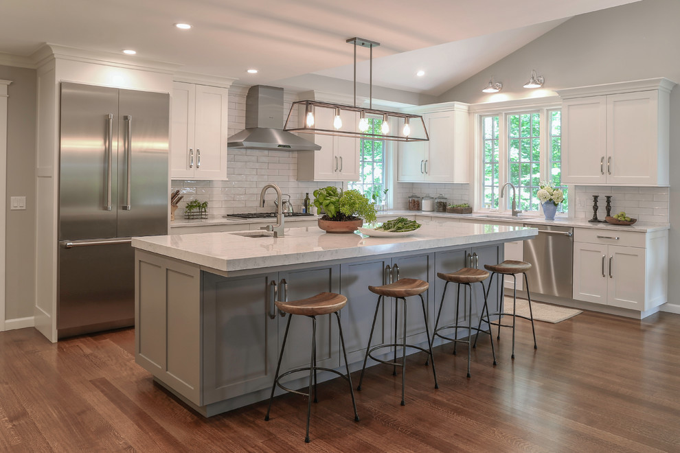 Example of a large transitional l-shaped medium tone wood floor eat-in kitchen design in Other with an undermount sink, shaker cabinets, quartz countertops, white backsplash, subway tile backsplash, stainless steel appliances, an island and white cabinets