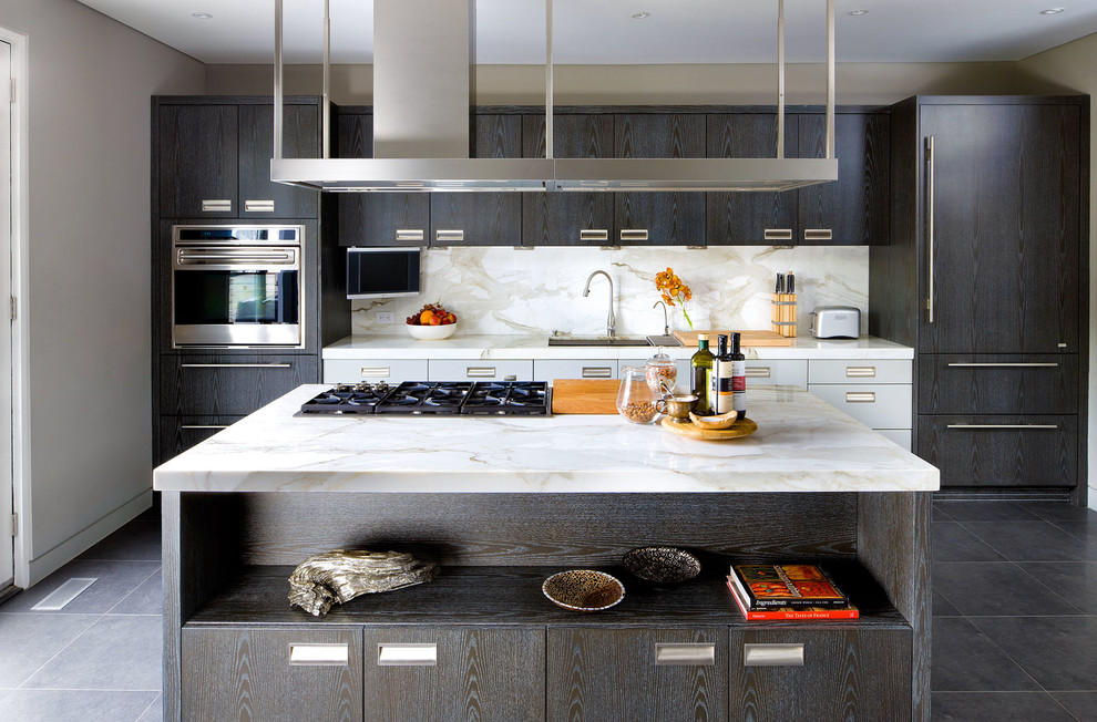 Photo of a contemporary galley kitchen in Toronto with a submerged sink, flat-panel cabinets, dark wood cabinets, white splashback, integrated appliances, an island and stone slab splashback.