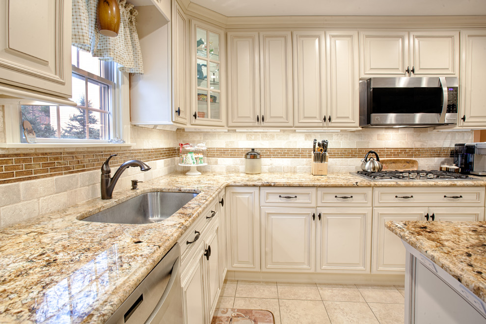 Eat-in kitchen - large traditional l-shaped porcelain tile and beige floor eat-in kitchen idea in New York with raised-panel cabinets, granite countertops, beige backsplash, stainless steel appliances, an island, an undermount sink, white cabinets and stone tile backsplash