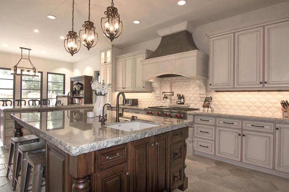 Eat-in kitchen - large mediterranean u-shaped ceramic tile eat-in kitchen idea in Sacramento with an undermount sink, raised-panel cabinets, white cabinets, granite countertops, white backsplash, porcelain backsplash, stainless steel appliances and an island