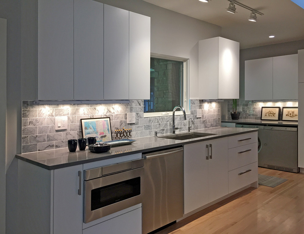 Bild på ett mellanstort funkis kök, med en undermonterad diskho, släta luckor, vita skåp, bänkskiva i kvarts, grått stänkskydd, stänkskydd i marmor, rostfria vitvaror och ljust trägolv