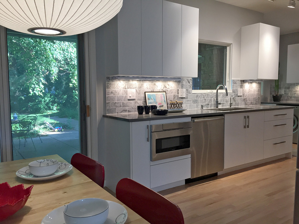 Photo of a medium sized contemporary galley kitchen/diner in Milwaukee with a submerged sink, flat-panel cabinets, white cabinets, engineered stone countertops, grey splashback, marble splashback, stainless steel appliances, light hardwood flooring and no island.