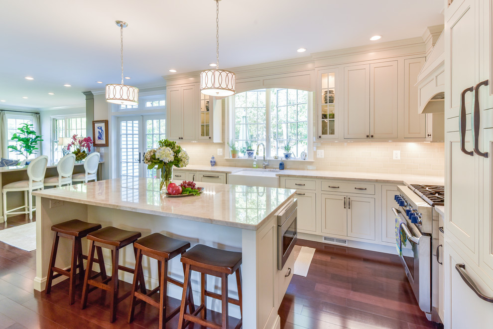 Large traditional l-shaped open plan kitchen in DC Metro with a submerged sink, beaded cabinets, white cabinets, engineered stone countertops, beige splashback, metro tiled splashback, stainless steel appliances, dark hardwood flooring, an island and brown floors.
