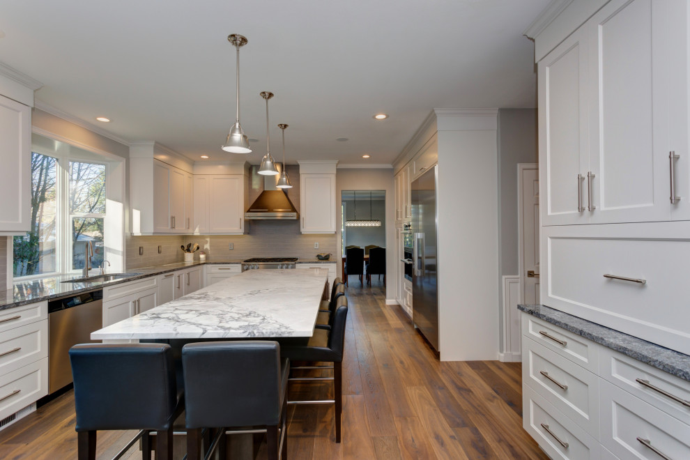 Inredning av ett klassiskt mellanstort grå grått kök, med en enkel diskho, luckor med infälld panel, grå skåp, granitbänkskiva, grått stänkskydd, stänkskydd i marmor, rostfria vitvaror, mellanmörkt trägolv, en köksö och brunt golv