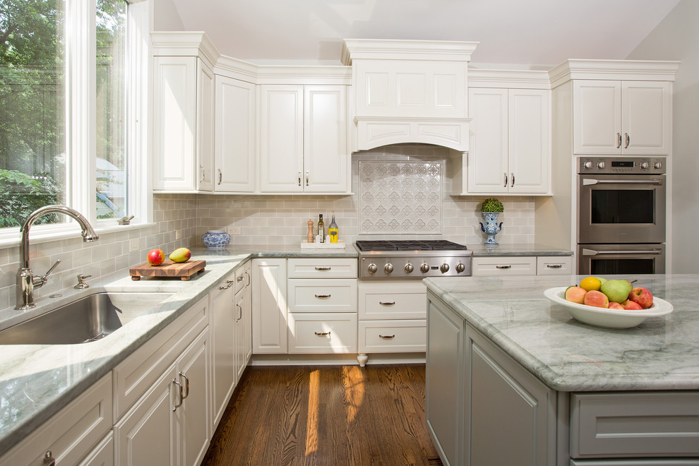Exempel på ett avskilt, stort klassiskt u-kök, med en undermonterad diskho, luckor med upphöjd panel, vita skåp, bänkskiva i kvartsit, grått stänkskydd, stänkskydd i keramik, rostfria vitvaror, mellanmörkt trägolv och en köksö