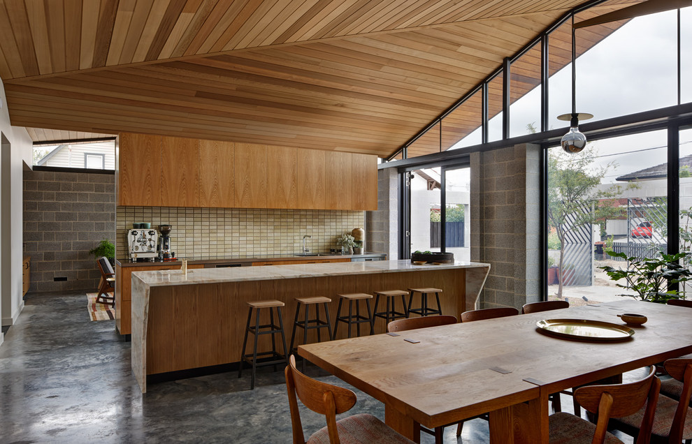 Mid-Century Wohnküche mit flächenbündigen Schrankfronten, hellbraunen Holzschränken, Küchenrückwand in Beige, Küchengeräten aus Edelstahl, Betonboden und Kücheninsel in Melbourne