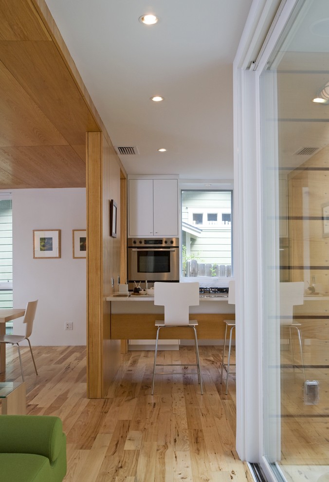 Пример оригинального дизайна: кухня-гостиная в стиле модернизм с плоскими фасадами, белыми фасадами и барной стойкой