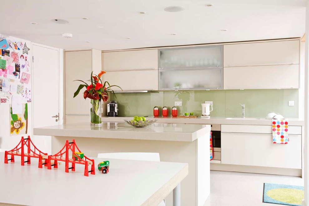Идея дизайна: параллельная кухня среднего размера в современном стиле с обеденным столом, врезной мойкой, плоскими фасадами, бежевыми фасадами, зеленым фартуком, фартуком из стекла, техникой из нержавеющей стали и островом