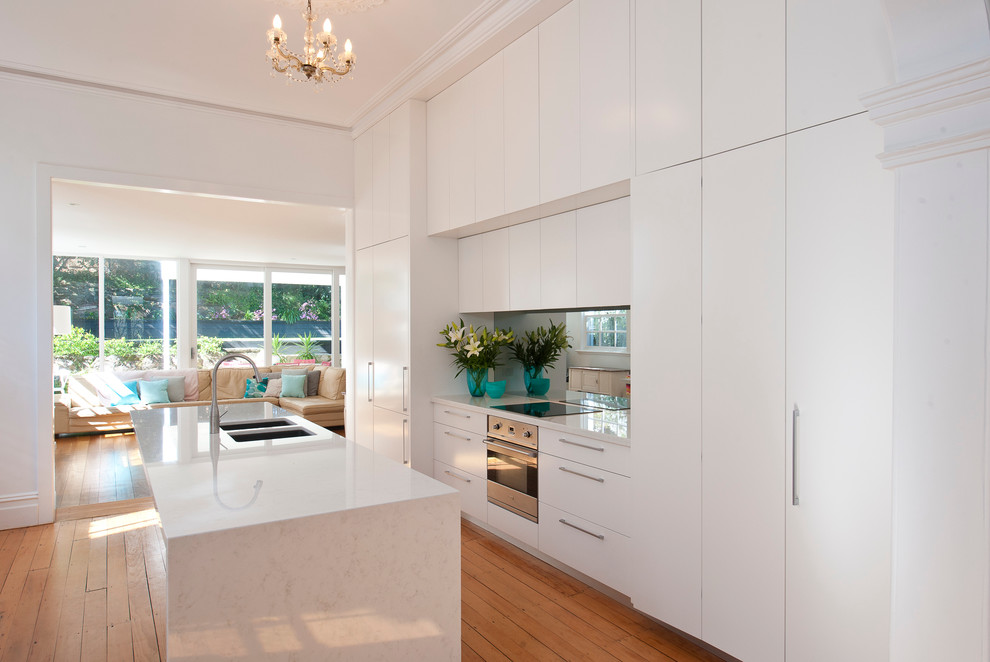 Zweizeilige Moderne Wohnküche mit Kücheninsel, Doppelwaschbecken, flächenbündigen Schrankfronten, weißen Schränken, Elektrogeräten mit Frontblende und braunem Holzboden in Sydney