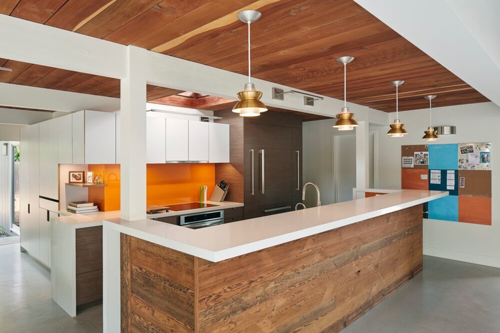 Идея дизайна: кухня в современном стиле с плоскими фасадами, белыми фасадами, оранжевым фартуком, фартуком из стекла, техникой под мебельный фасад и бетонным полом