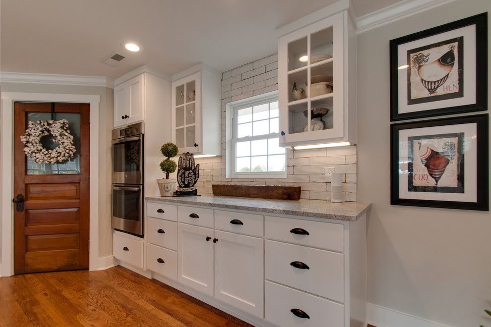 Inredning av ett lantligt stort grå grått kök, med en undermonterad diskho, skåp i shakerstil, vita skåp, marmorbänkskiva, vitt stänkskydd, stänkskydd i keramik, rostfria vitvaror, mellanmörkt trägolv, flera köksöar och brunt golv