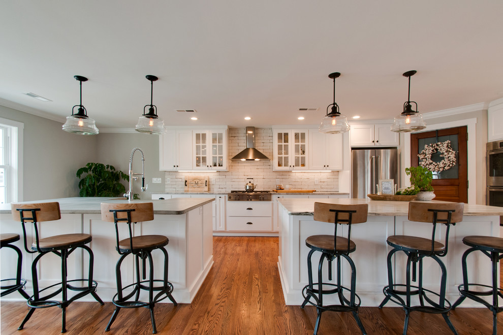 Example of a large farmhouse l-shaped medium tone wood floor and brown floor open concept kitchen design in Nashville with an undermount sink, shaker cabinets, white cabinets, marble countertops, white backsplash, ceramic backsplash, stainless steel appliances, two islands and gray countertops