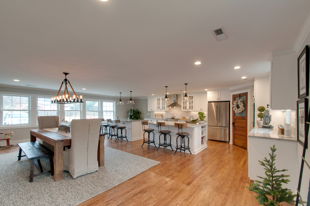 Photo of a large country l-shaped open plan kitchen in Nashville with a submerged sink, shaker cabinets, white cabinets, marble worktops, white splashback, ceramic splashback, stainless steel appliances, medium hardwood flooring, multiple islands, brown floors and grey worktops.