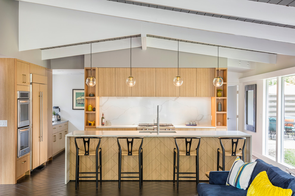 This is an example of a midcentury open plan kitchen in Kansas City with a submerged sink, flat-panel cabinets, light wood cabinets, white splashback, stone slab splashback, integrated appliances, an island, brown floors and white worktops.