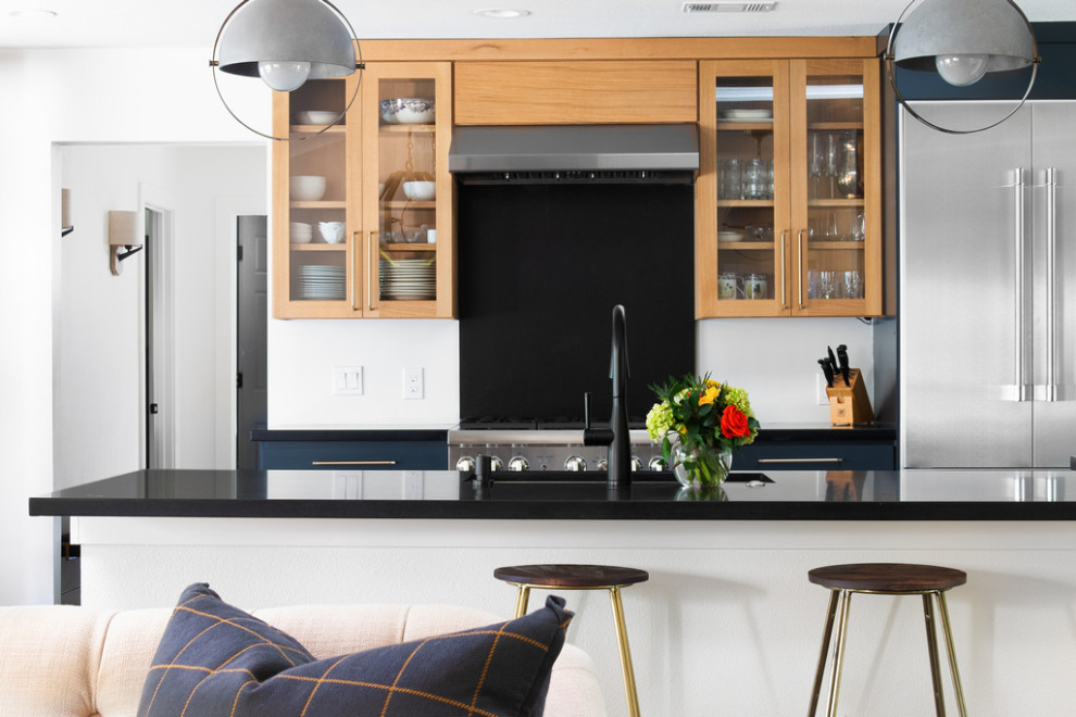 На фото: параллельная кухня-гостиная среднего размера в стиле неоклассика (современная классика) с врезной мойкой, плоскими фасадами, синими фасадами, техникой из нержавеющей стали, полуостровом и черной столешницей