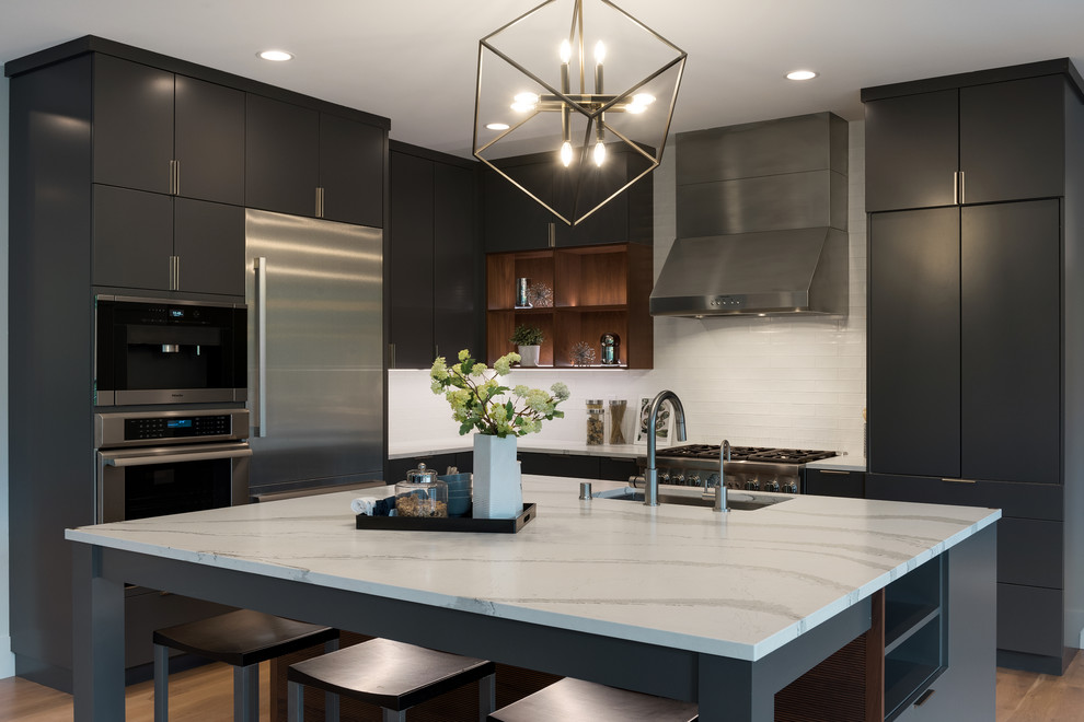 Moderne Küche in L-Form mit Unterbauwaschbecken, flächenbündigen Schrankfronten, schwarzen Schränken, Küchenrückwand in Weiß, Küchengeräten aus Edelstahl, dunklem Holzboden, Kücheninsel und braunem Boden in Minneapolis