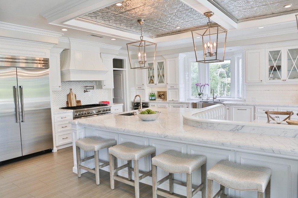 Inspiration for a large transitional l-shaped porcelain tile and gray floor eat-in kitchen remodel in San Diego with a farmhouse sink, raised-panel cabinets, white cabinets, marble countertops, white backsplash, marble backsplash, stainless steel appliances and an island
