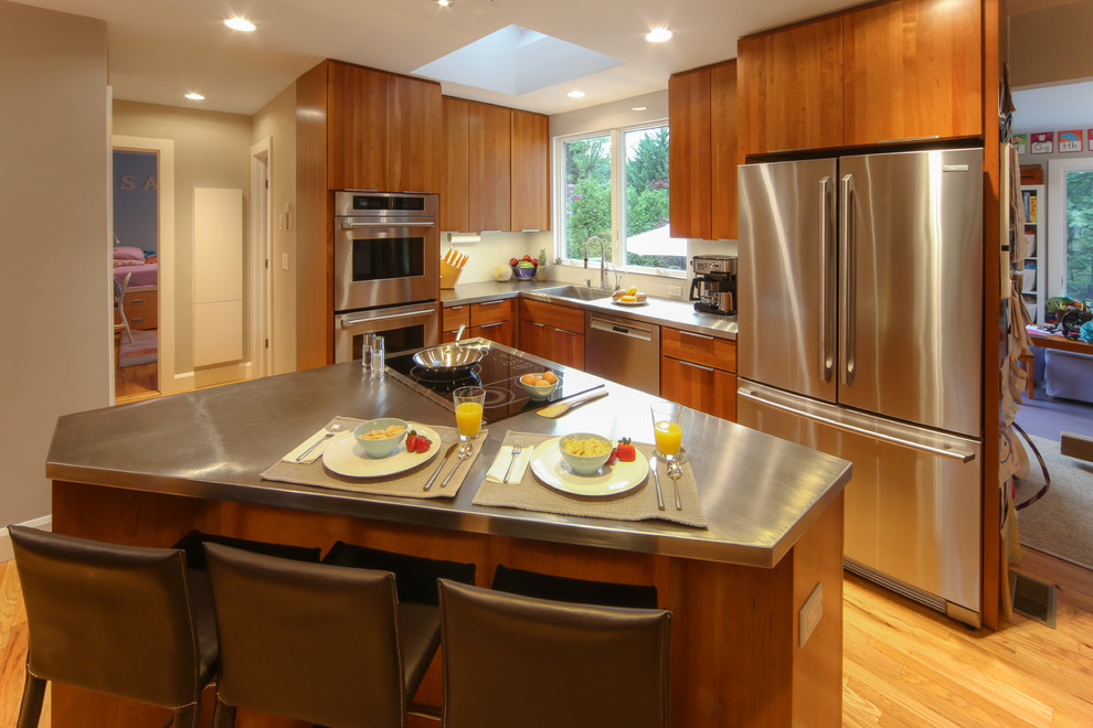 Example of a small minimalist l-shaped light wood floor and brown floor eat-in kitchen design in New York with an integrated sink, flat-panel cabinets, brown cabinets, stainless steel countertops, white backsplash, glass sheet backsplash, stainless steel appliances and an island