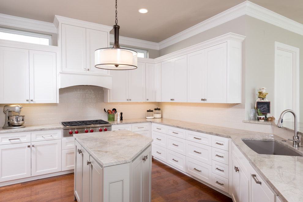 Example of a mid-sized transitional l-shaped medium tone wood floor enclosed kitchen design in Dallas with an undermount sink, shaker cabinets, white cabinets, quartzite countertops, white backsplash, ceramic backsplash, stainless steel appliances and an island