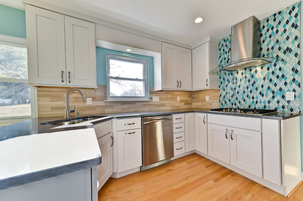 L-shaped enclosed kitchen photo with an undermount sink, recessed-panel cabinets, white cabinets, quartzite countertops, multicolored backsplash, mosaic tile backsplash and stainless steel appliances