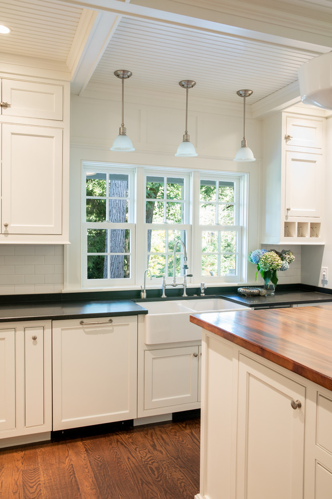 Country medium tone wood floor and brown floor eat-in kitchen photo in Portland Maine with a farmhouse sink, shaker cabinets, white cabinets, white backsplash and an island
