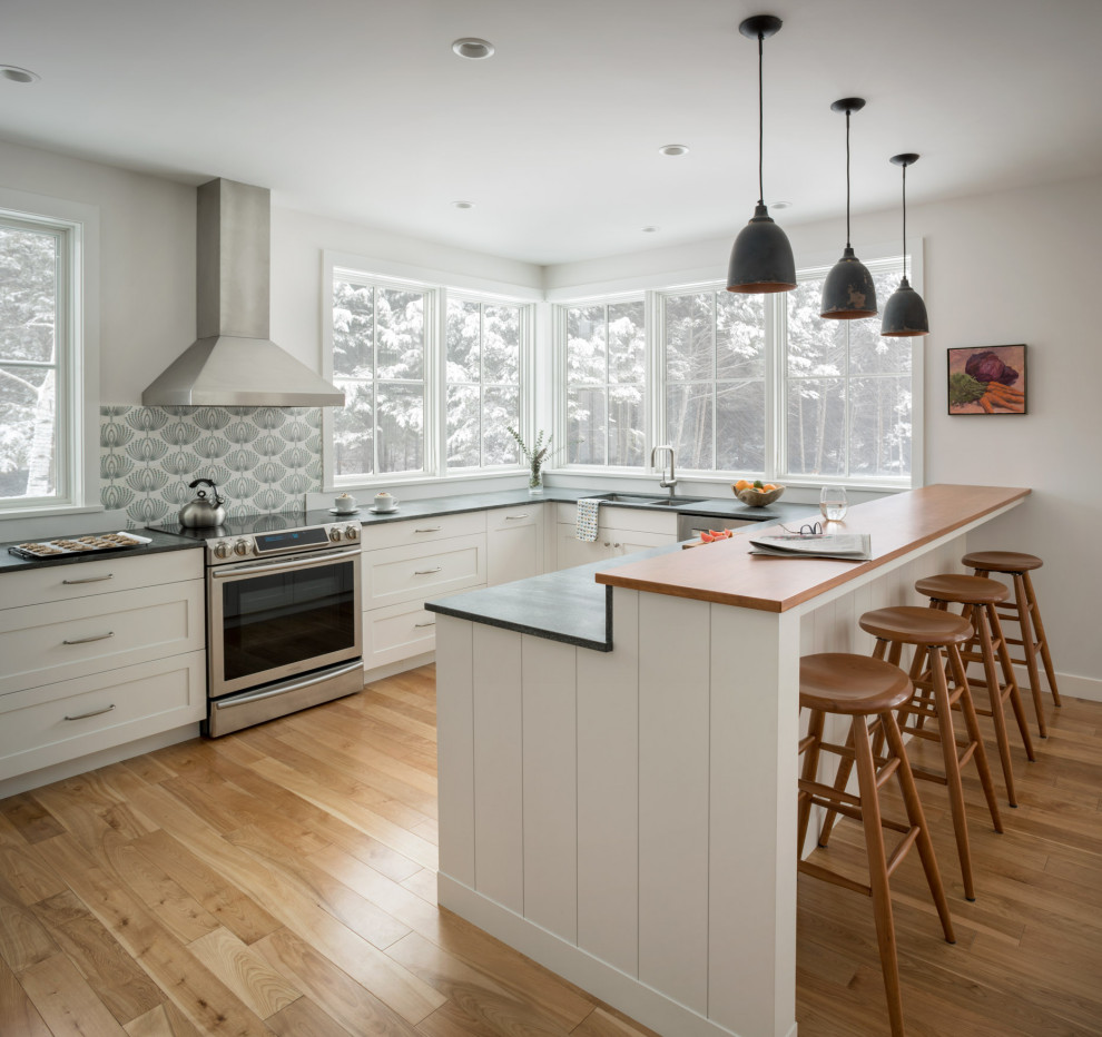 Kitchen - mid-sized cottage u-shaped medium tone wood floor and brown floor kitchen idea in Portland Maine with an undermount sink, shaker cabinets, white cabinets, granite countertops, white backsplash, ceramic backsplash, stainless steel appliances, a peninsula and gray countertops