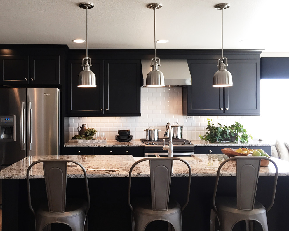 Eat-in kitchen - mid-sized transitional l-shaped light wood floor eat-in kitchen idea in Denver with a farmhouse sink, recessed-panel cabinets, black cabinets, granite countertops, white backsplash, ceramic backsplash, stainless steel appliances and an island